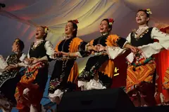 Танцьорки в български народни носии с цветя в косите играят хоро на сцена под шатра